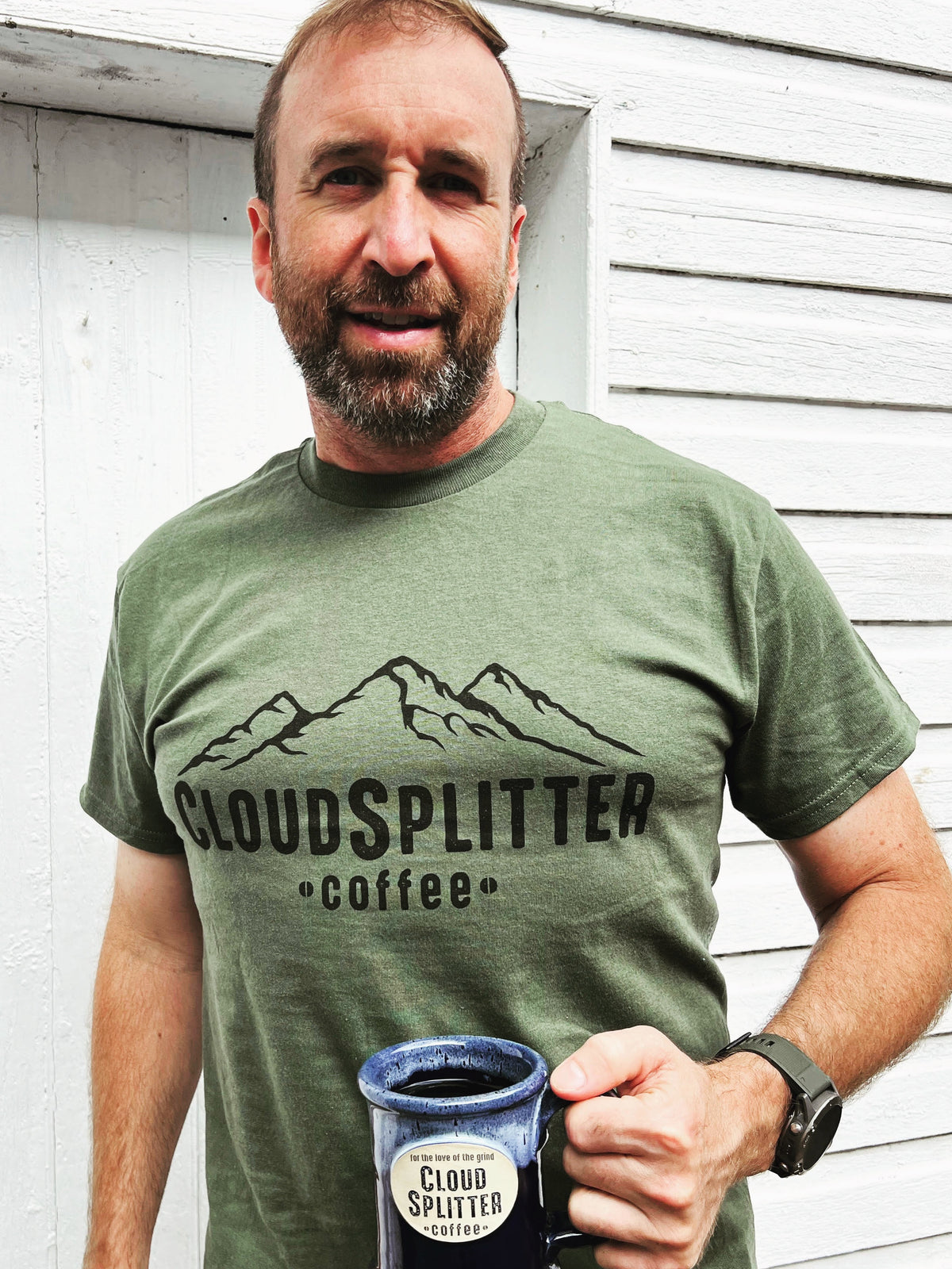 Man wearing a green t-shirt with 'Cloudsplitter Coffee' logo, holding a coffee cup.